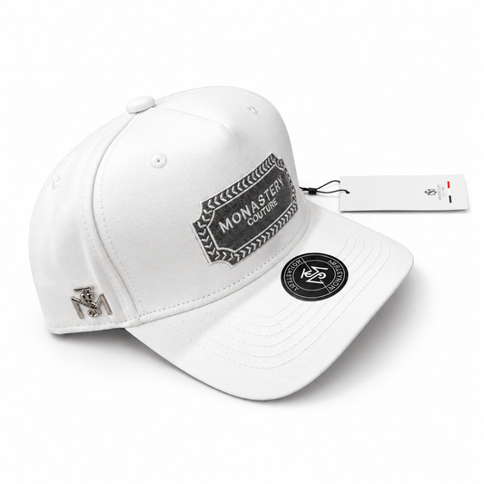 Gorra Monastery blanca con parche bordado gris y emblema metálico lateral en fondo blanco