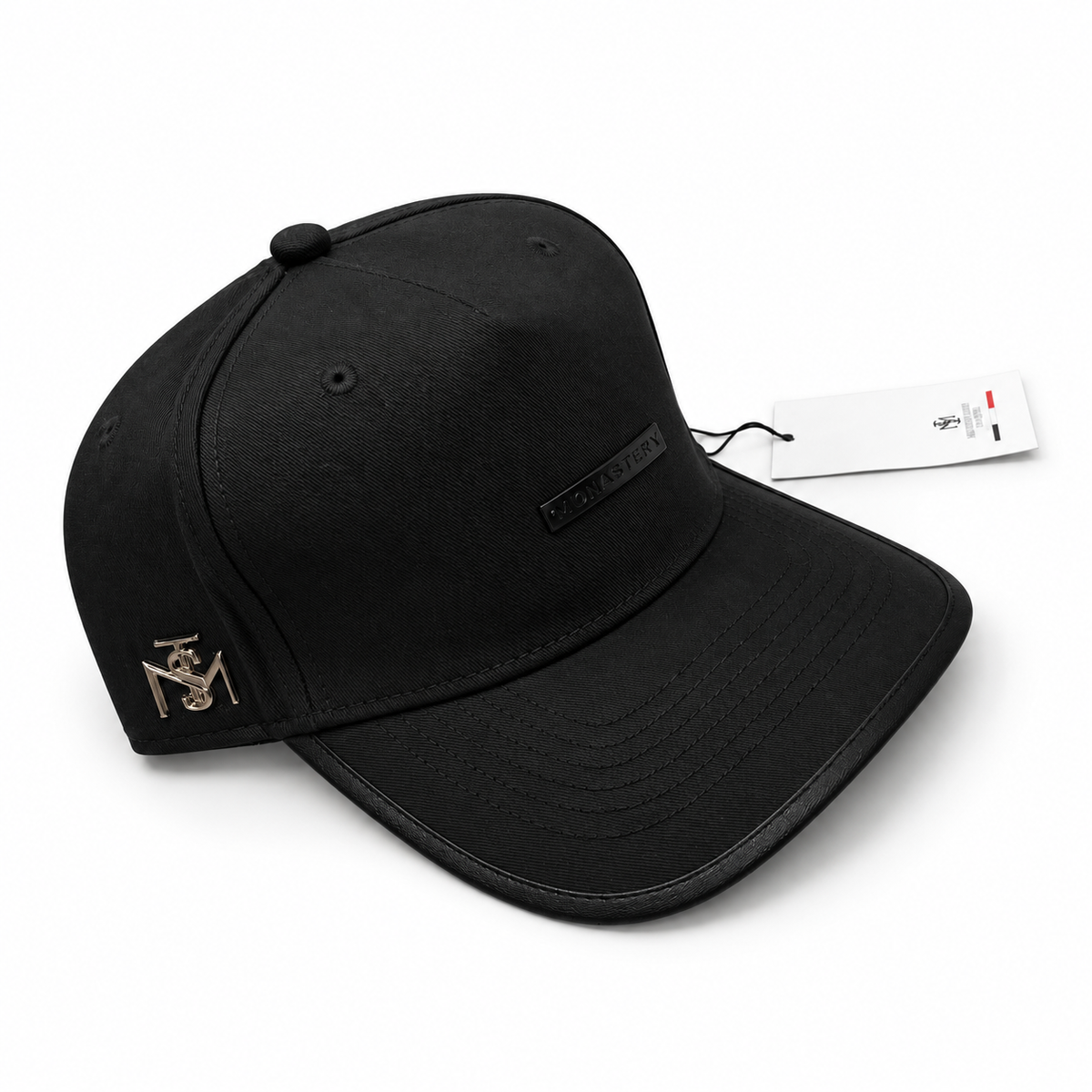 Gorra Monastery Full Black con placa negra y emblema metálico lateral en fondo blanco