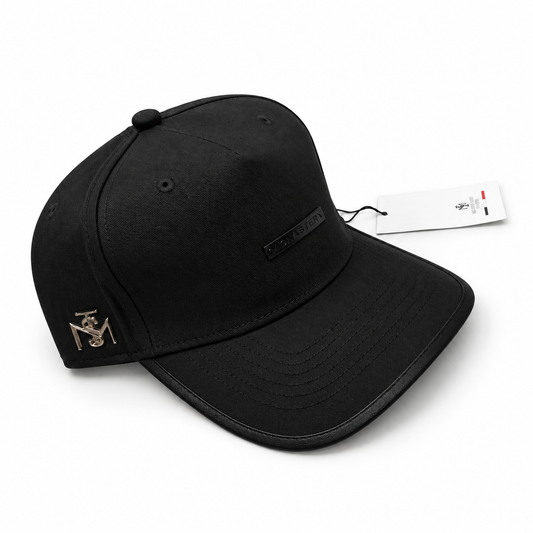 Gorra Monastery Full Black con placa negra y emblema metálico lateral en fondo blanco